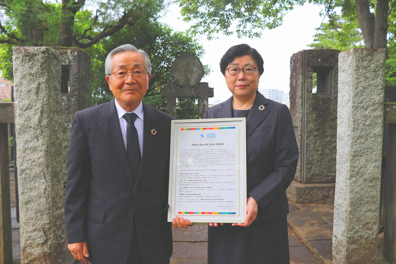 写真：創立者・井上円了の墓前で憲章を掲げる安齋理事長と矢口学長